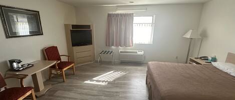 Una habitación de hotel con cama, escritorio con silla, televisión y ventana con cortinas.