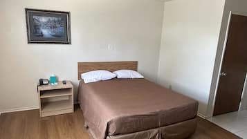 Un dormitorio con cama, mesita de noche, un cuadro enmarcado en la pared y una puerta.