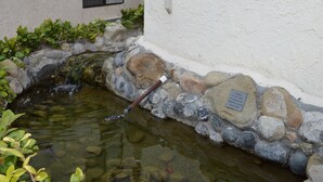 A small pond with a wooden bridge, surrounded by rocks and plants, next to a building with a stone wall and a window. - Jolly Roger Hotel (Marina del Rey)