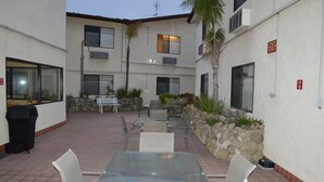 An outdoor patio area with a glass table and chairs, surrounded by stone walls and plants. - Jolly Roger Hotel (Marina del Rey)