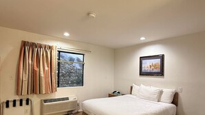 A bedroom with a bed, a window with curtains, a radiator, and a painting on the wall. - Jolly Roger Hotel (Marina del Rey)