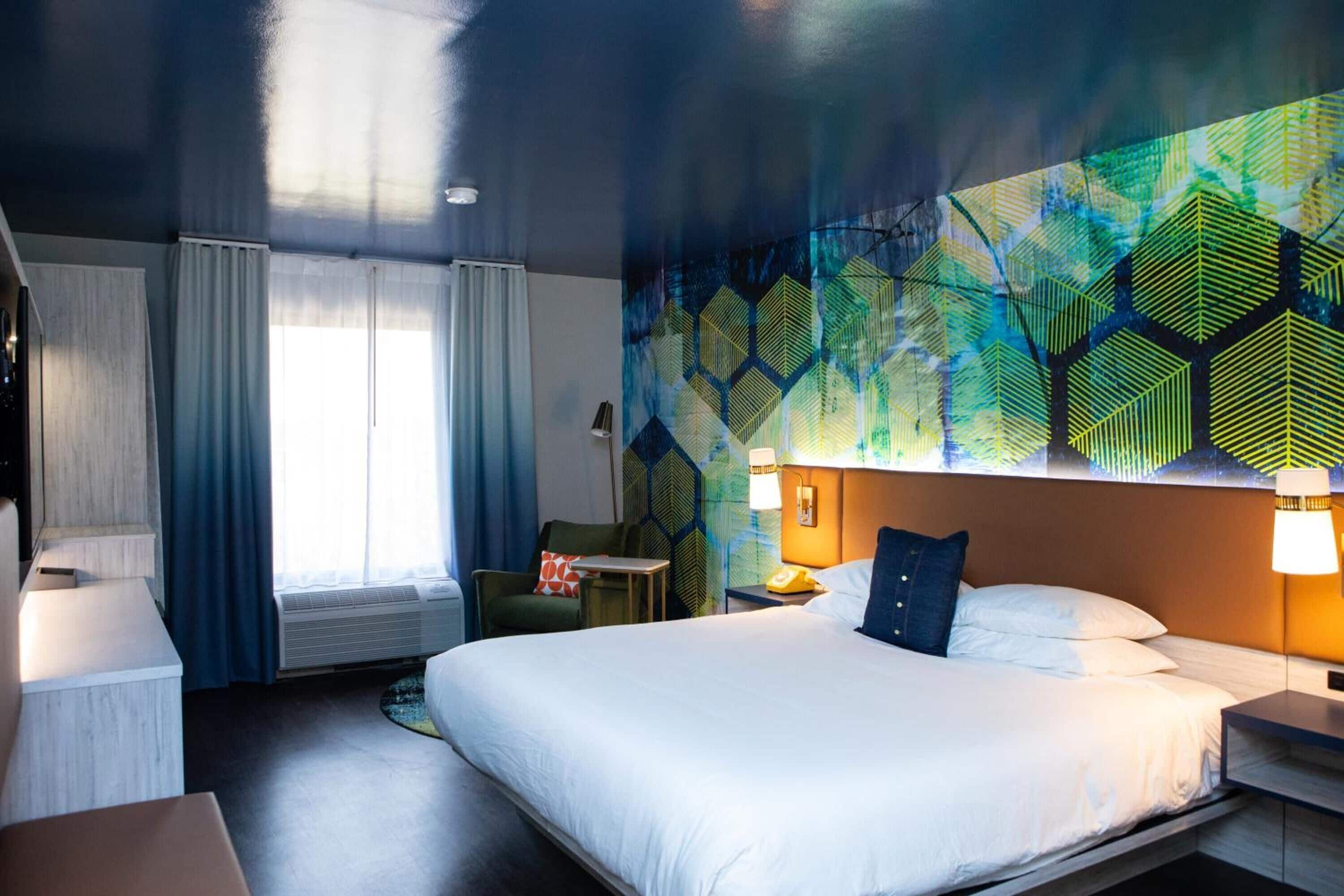 A hotel room with a large bed, a desk, a chair, and a wall mural.