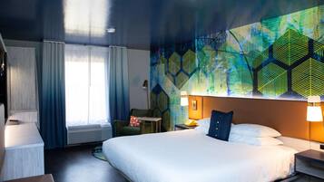 A hotel room with a large bed, a desk, a chair, and a wall mural.