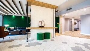 A modern lobby with a white brick wall, wooden reception desk, green stools, and a hexagonal patterned floor. - Hotel Denim (Greensboro)
