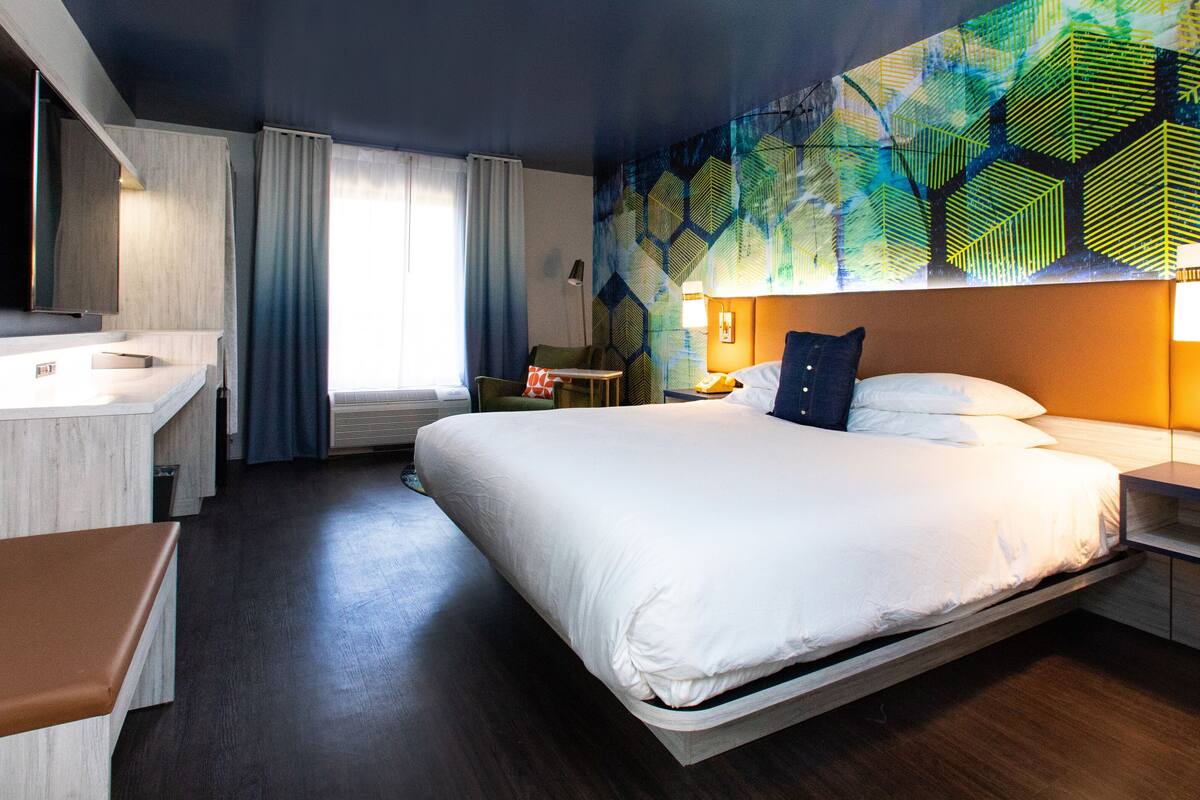 A hotel room with a large bed, a desk, a chair, and a wall with a geometric pattern.