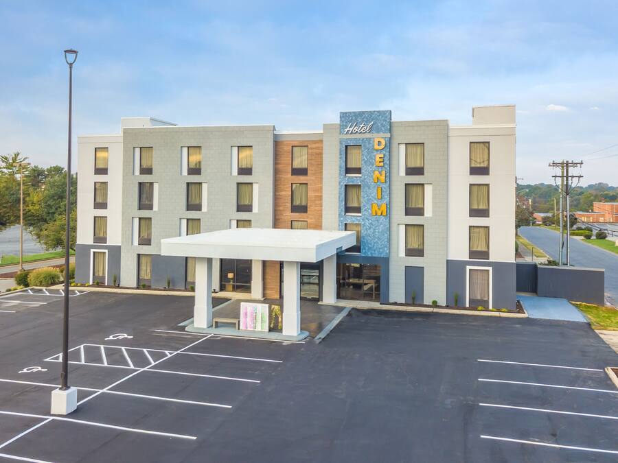 Um hotel com design moderno, exibindo uma placa chamativa do 'Hotel DENIM', uma entrada coberta e um estacionamento.