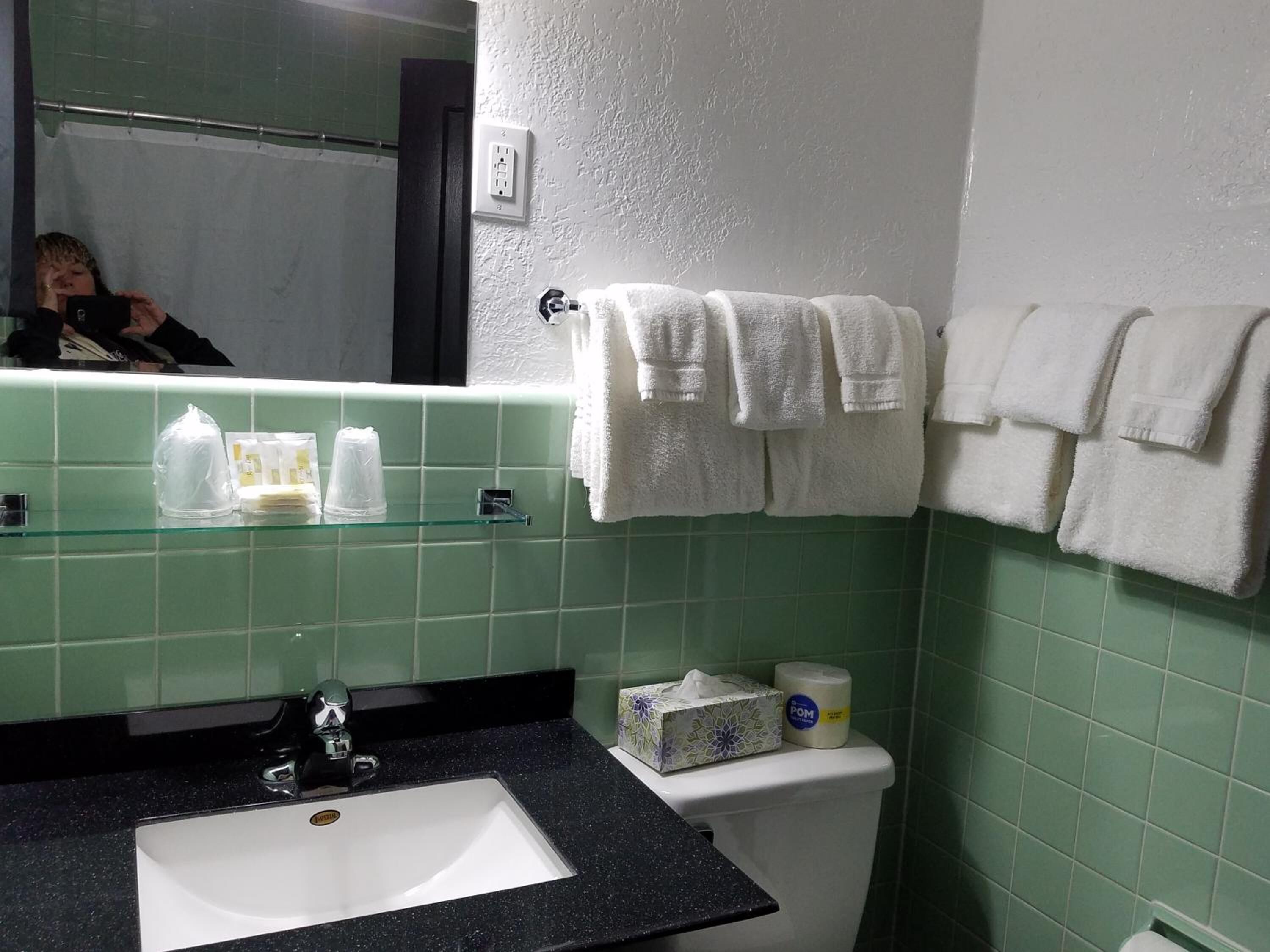 Une salle de bain avec un lavabo blanc, des murs recouverts de carreaux verts et plusieurs serviettes blanches suspendues à un porte-serviettes.