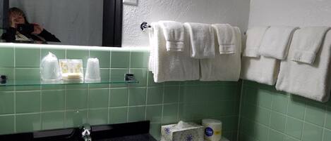 Une salle de bain avec un lavabo blanc, des murs recouverts de carreaux verts et plusieurs serviettes blanches suspendues à un porte-serviettes.
