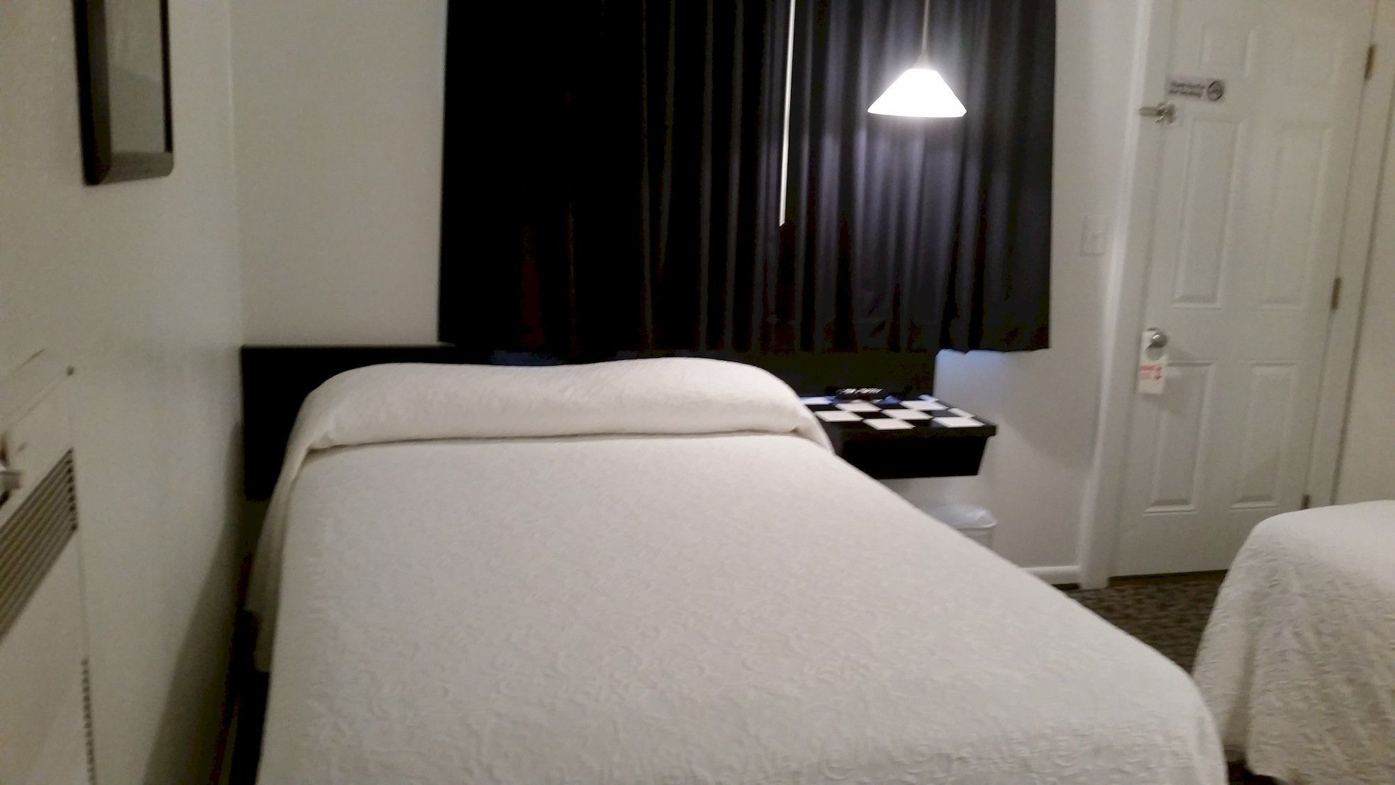 A hotel room with a single bed, a small bedside table, a nightstand, a window with curtains, and a door.