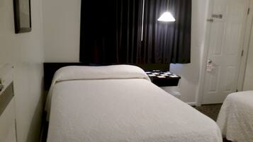A hotel room with a single bed, a small bedside table, a nightstand, a window with curtains, and a door.