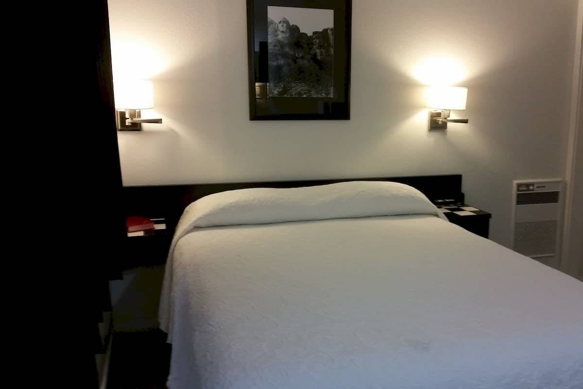 A hotel room with a bed, two bedside lamps, a framed picture on the wall, and a heater on the wall.