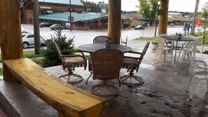 An outdoor patio with wicker furniture, a wooden bench, and a view of a restaurant and street.