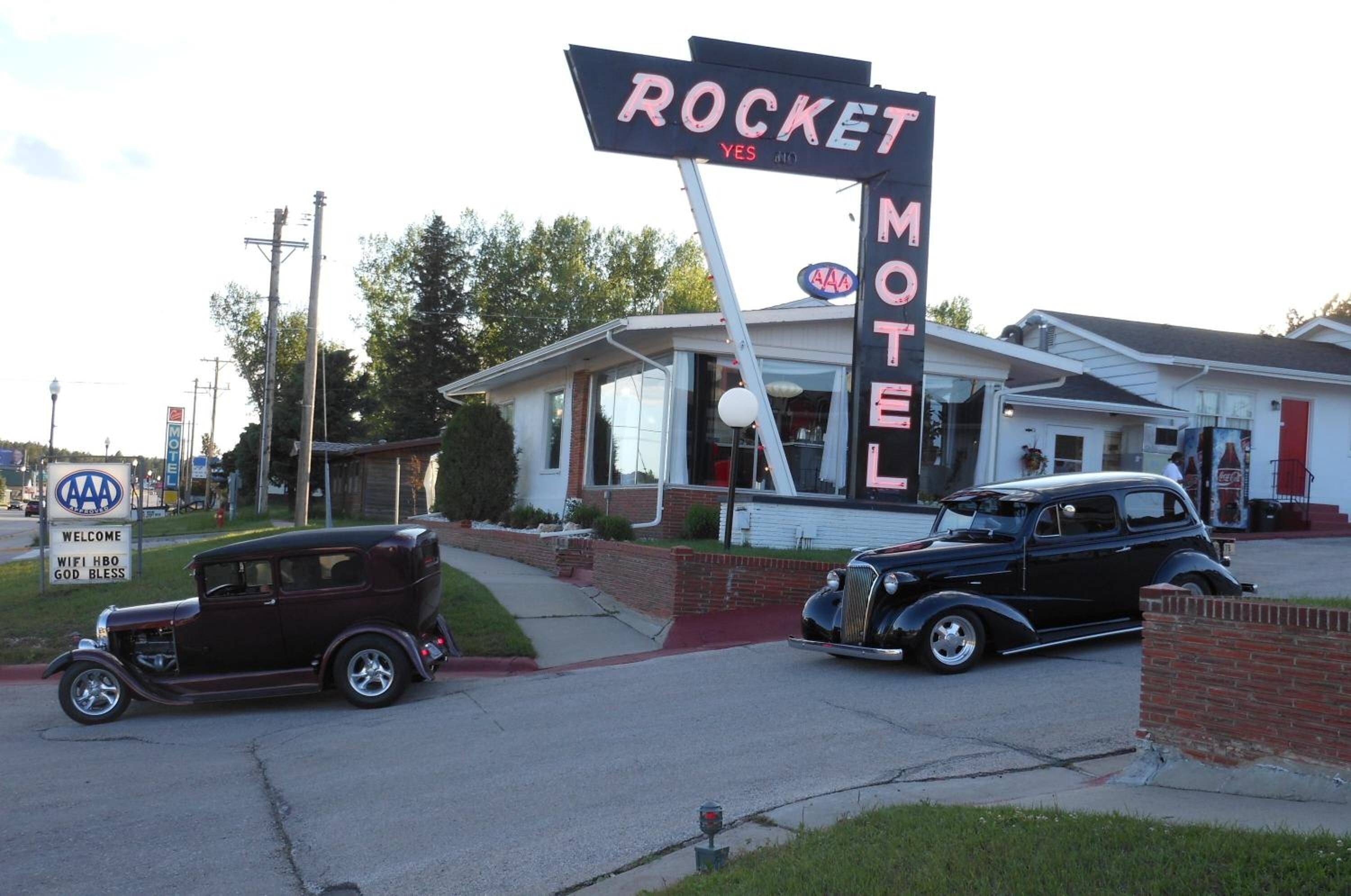 Un coche antiguo estacionado frente a un motel llamado 'Rocket Motel'.