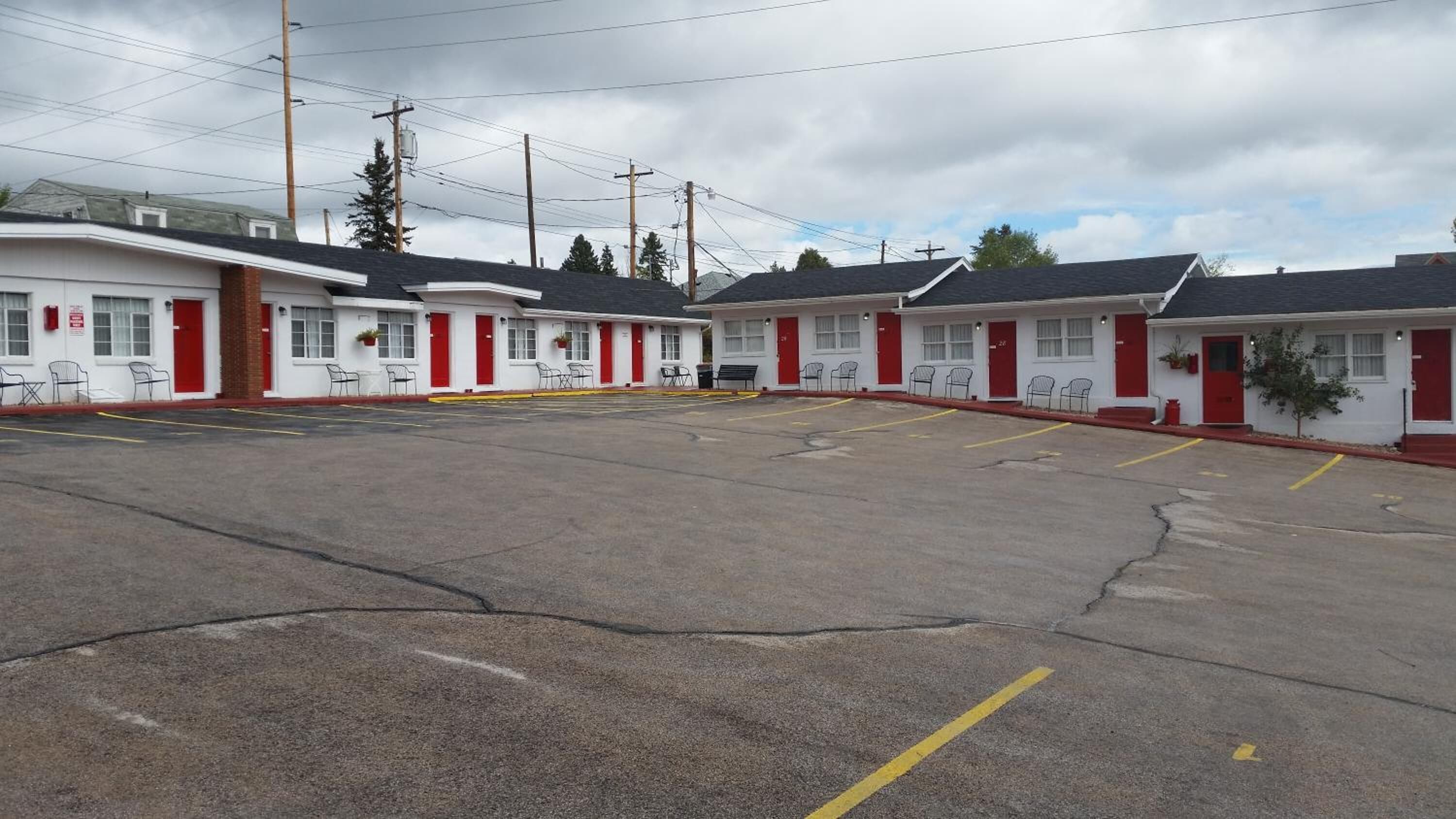Une rangée de bâtiments d’un seul étage, typiques des motels, avec des portes rouges et des façades blanches, un parking avec des places délimitées et des poteaux électriques au-dessus.