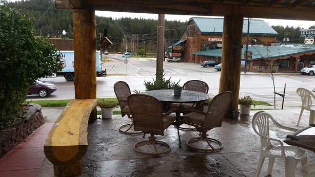 An outdoor patio with wicker chairs and a wooden table, overlooking a street with a restaurant named 'Cattleman's Steak BBQ' in the background. - Rocket Motel (Custer)
