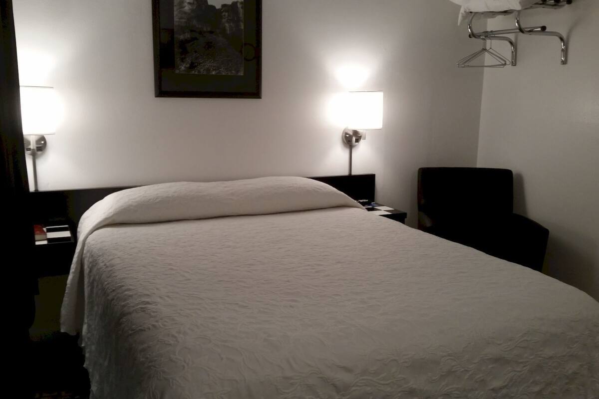 A hotel room with a neatly made bed, two bedside lamps, a chair, and a small table with a lamp.