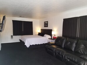 A hotel room with a bed, a black leather sofa, a TV mounted on the wall, and two bedside lamps.