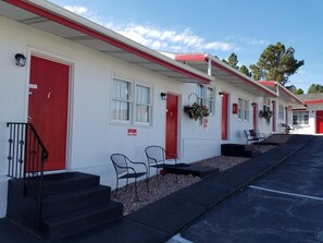 A motel with red doors and windows, outdoor seating, and a parking lot.