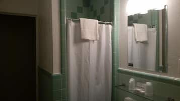 Baño con cortina blanca de ducha, repisa de vidrio con artículos de aseo y espejo que refleja la zona de la ducha.