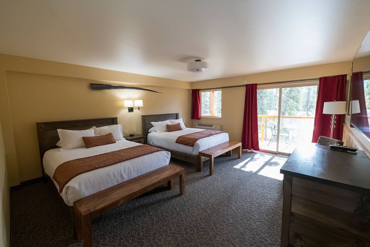 A hotel room with two beds, a desk, and a view of the outdoors.