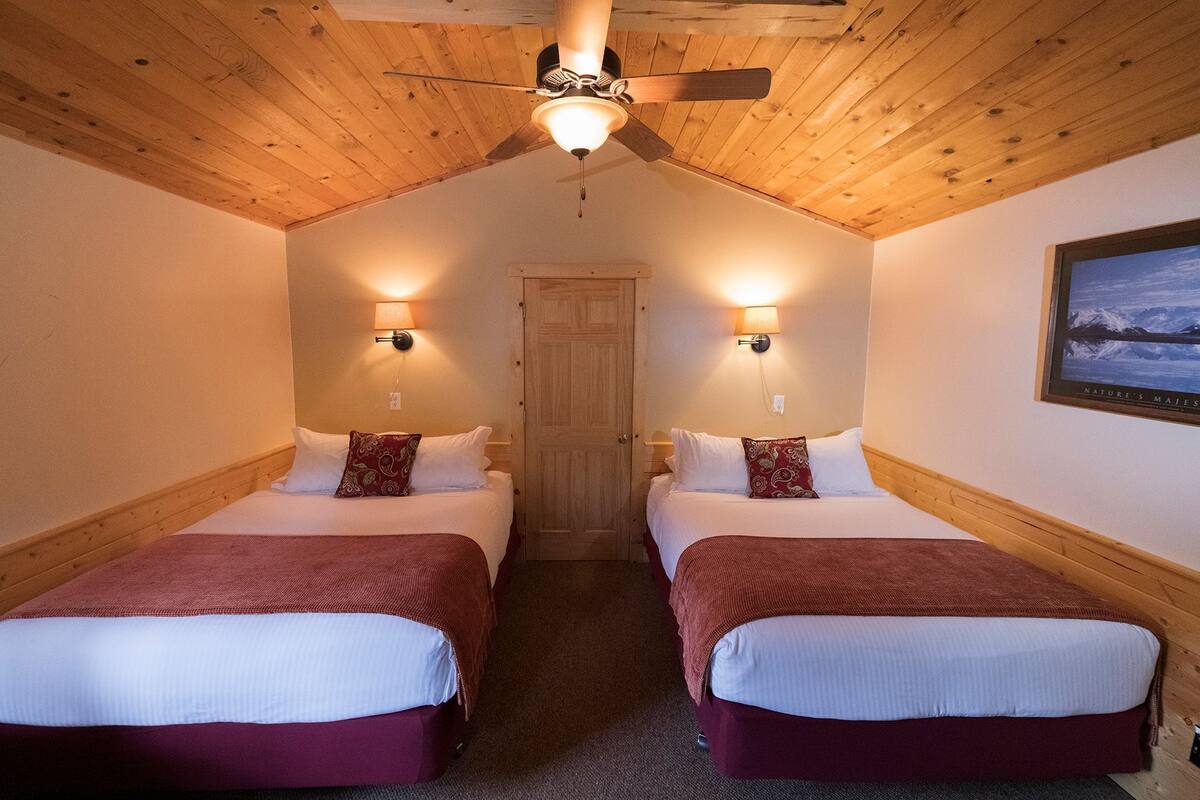 A room with two beds, wooden ceiling, and a ceiling fan.