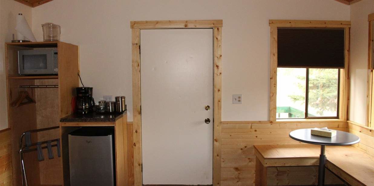 A compact kitchen with a microwave, coffee maker, and refrigerator. There's a door with a window and a small table with a box on it.
