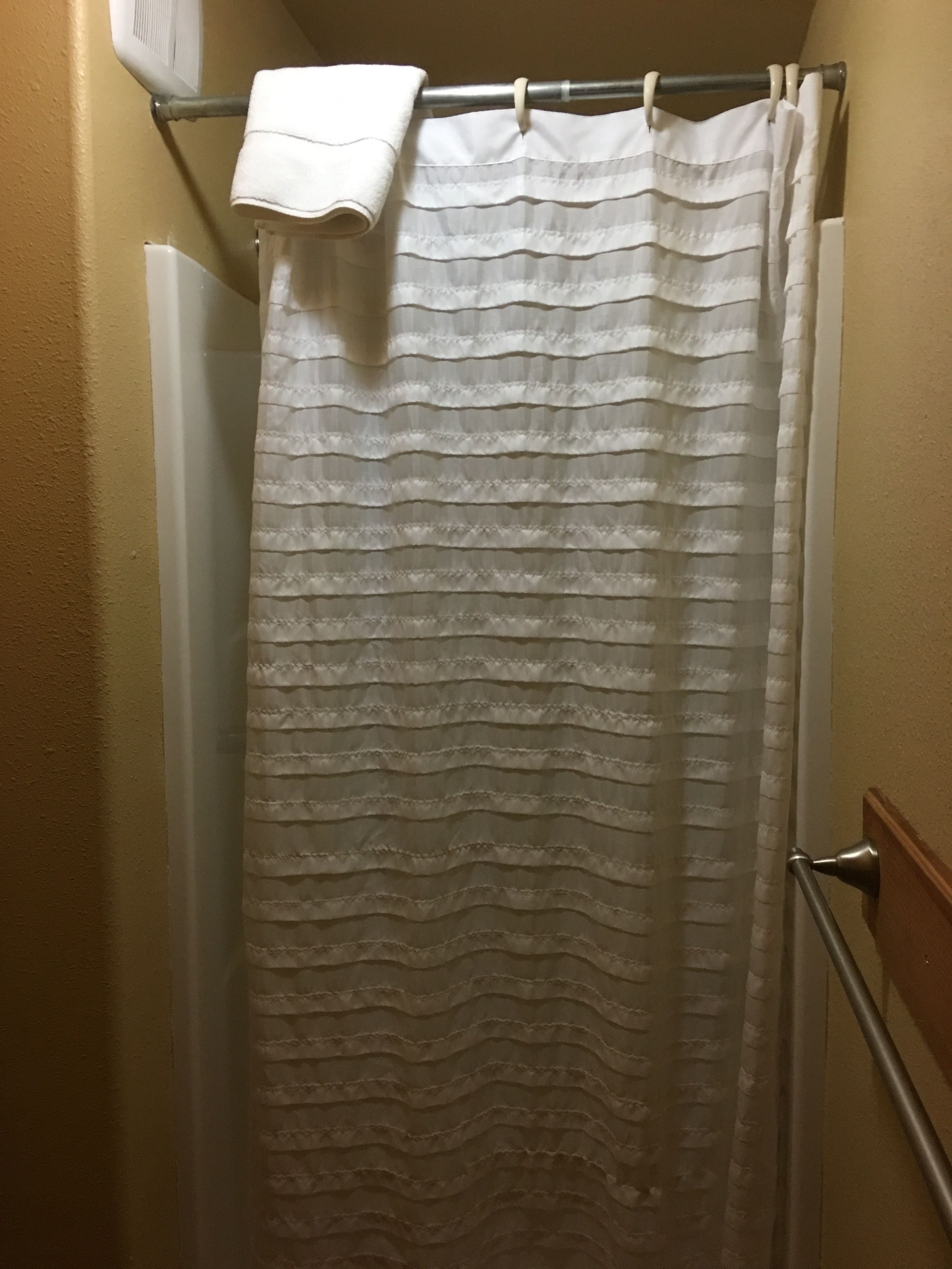 Une salle de bain avec un rideau de douche, une serviette accrochée au mur et un pommeau de douche.