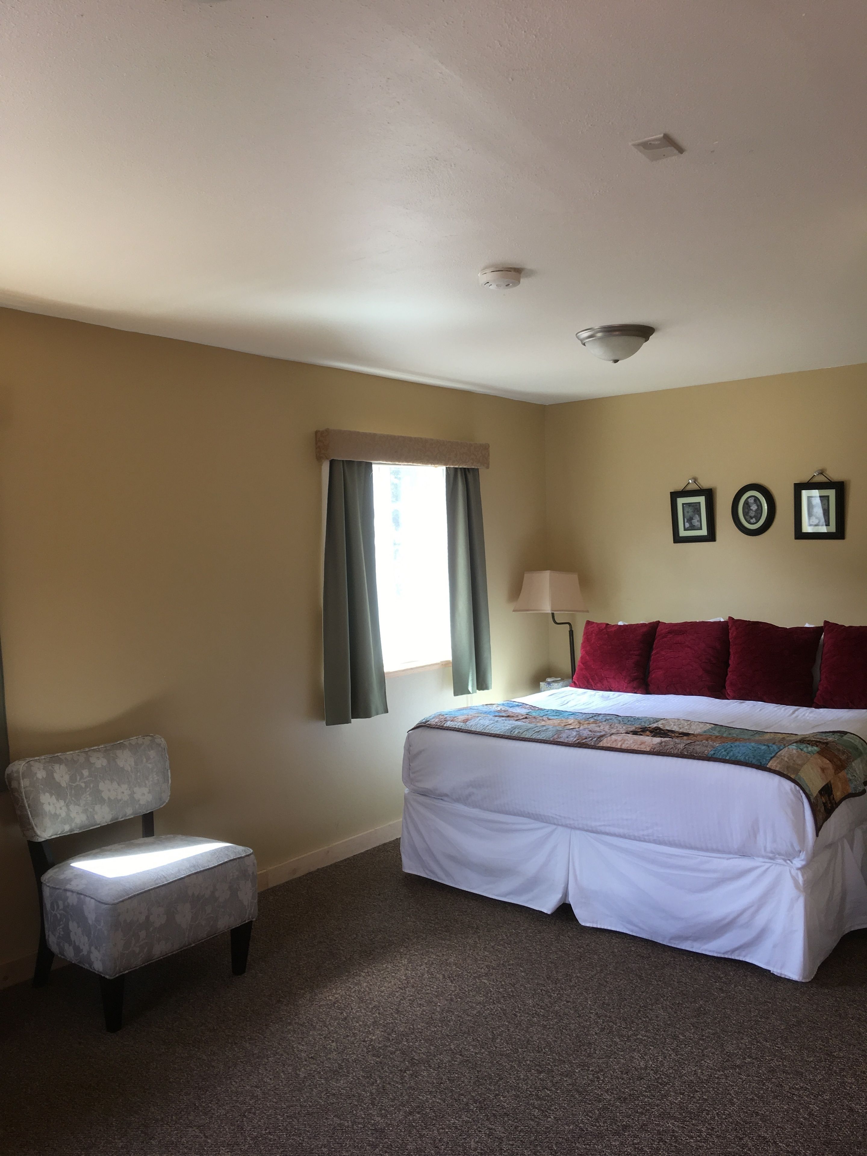 A hotel room with a bed, a chair, a window with curtains, and a ceiling light.