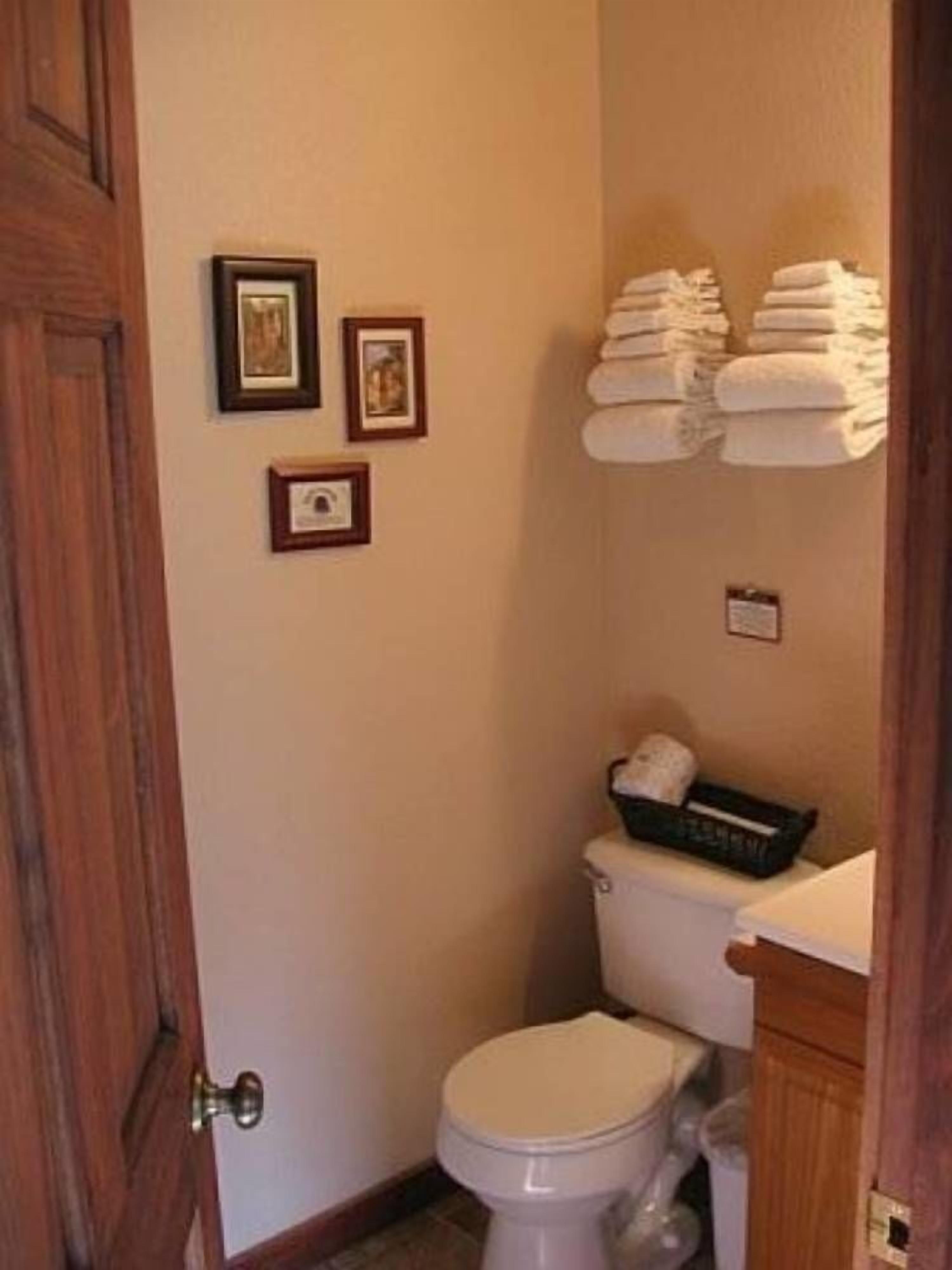 Une petite salle de bain avec des toilettes, un lavabo et une étagère où sont pliées des serviettes. Trois tableaux encadrés ornent le mur.