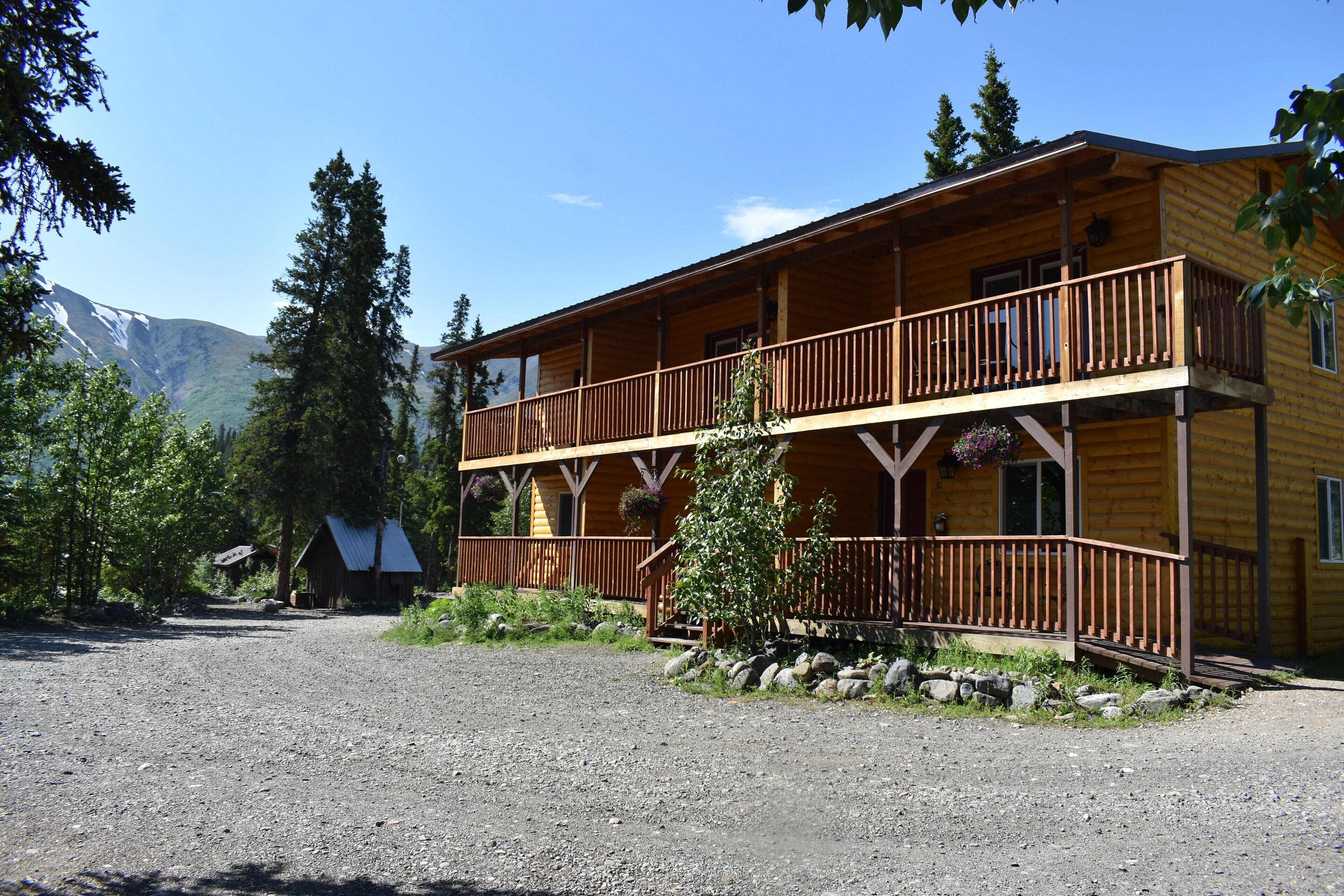 Un chalet en bois à deux étages, doté d’un balcon, entouré d’arbres et avec une montagne en arrière-plan.