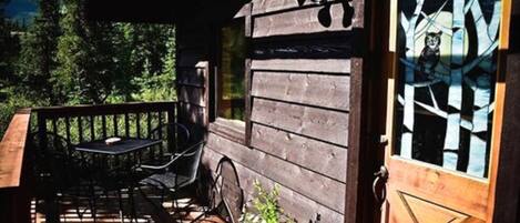 A wooden cabin with a deck, a table, and chairs.