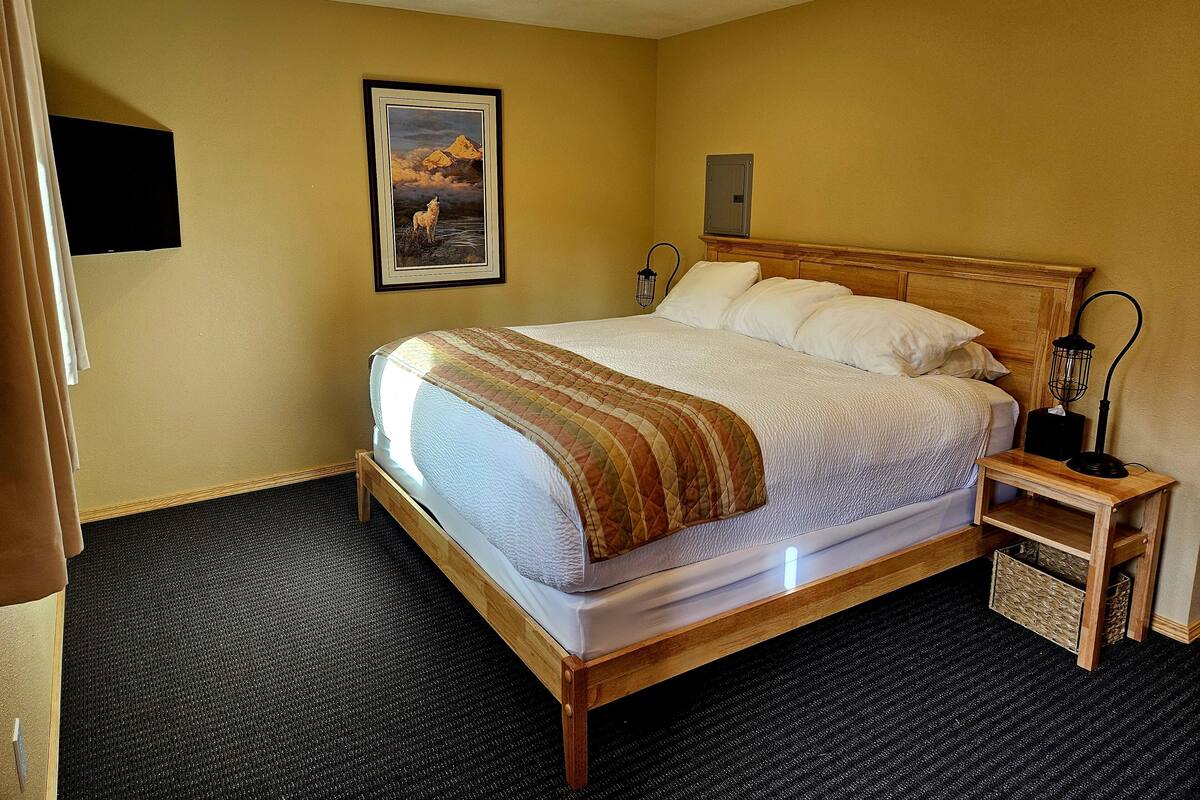 A hotel room with a large bed, a nightstand with a lamp, a picture on the wall, and a carpeted floor.