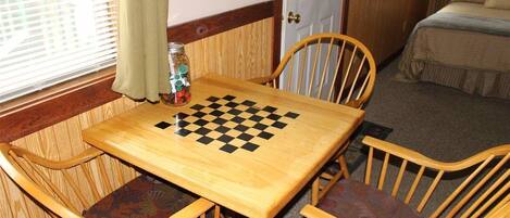 A wooden table with a checkered game board, surrounded by wooden chairs with cushioned seats.