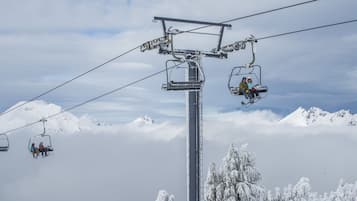 En skilift med stole, der transporterer skiløbere foran sneklædte bjerge og træer.