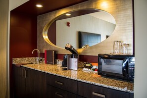 A modern kitchen with granite countertops, a built-in microwave, a coffee machine, and a large mirror above the sink.