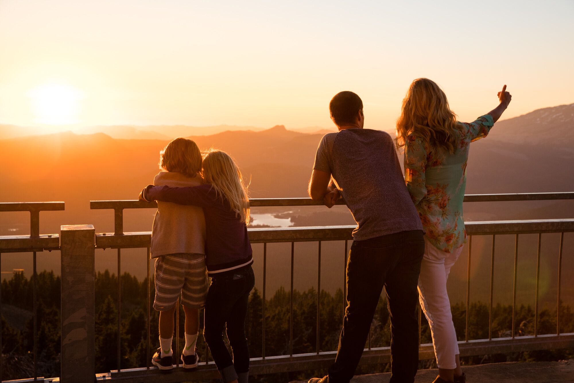 A group of people standing on a balcony overlooking a sunset with mountains in the background.