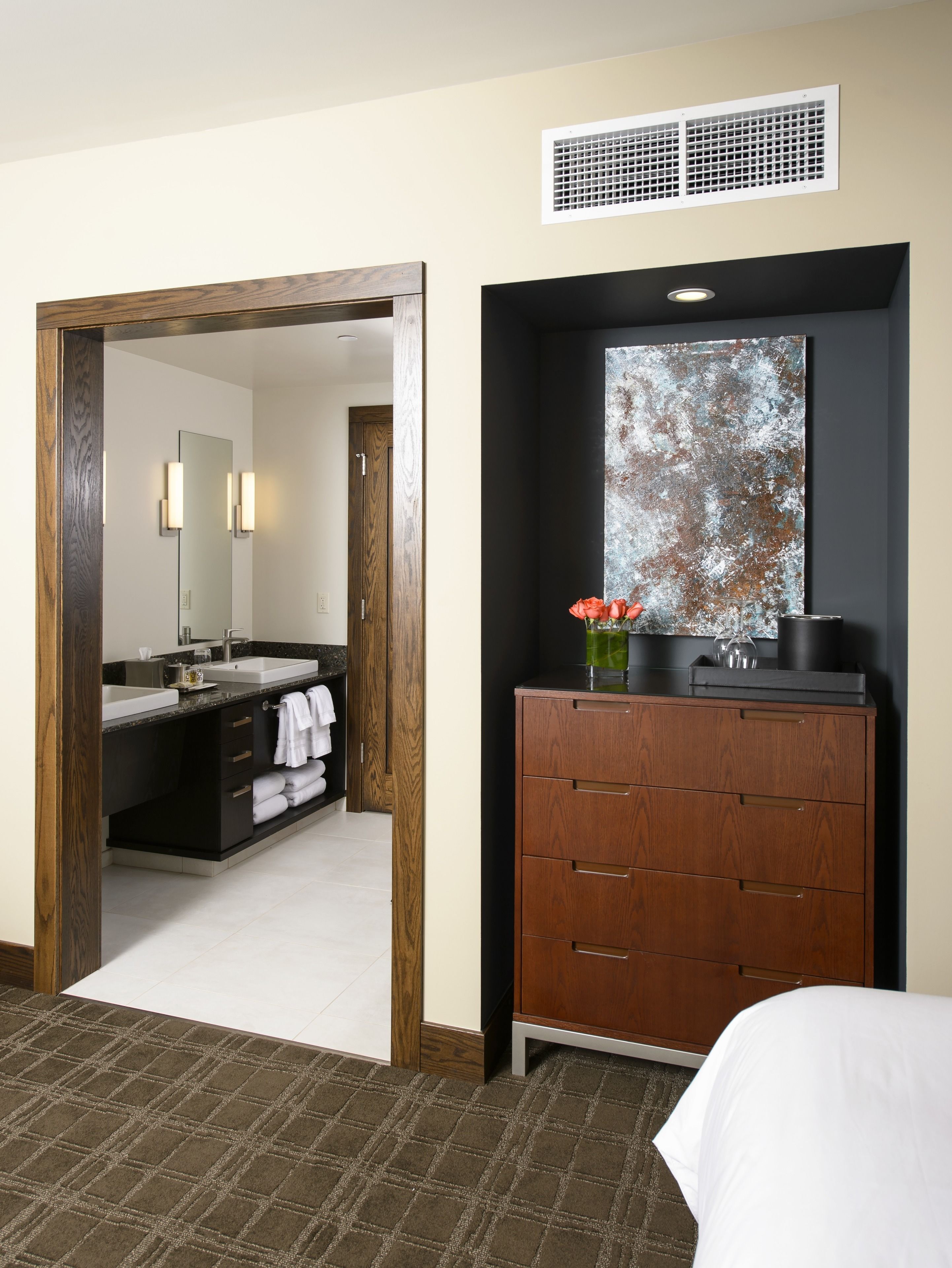A hotel room with a wooden wardrobe, a large mirror, a sink, and a bed.