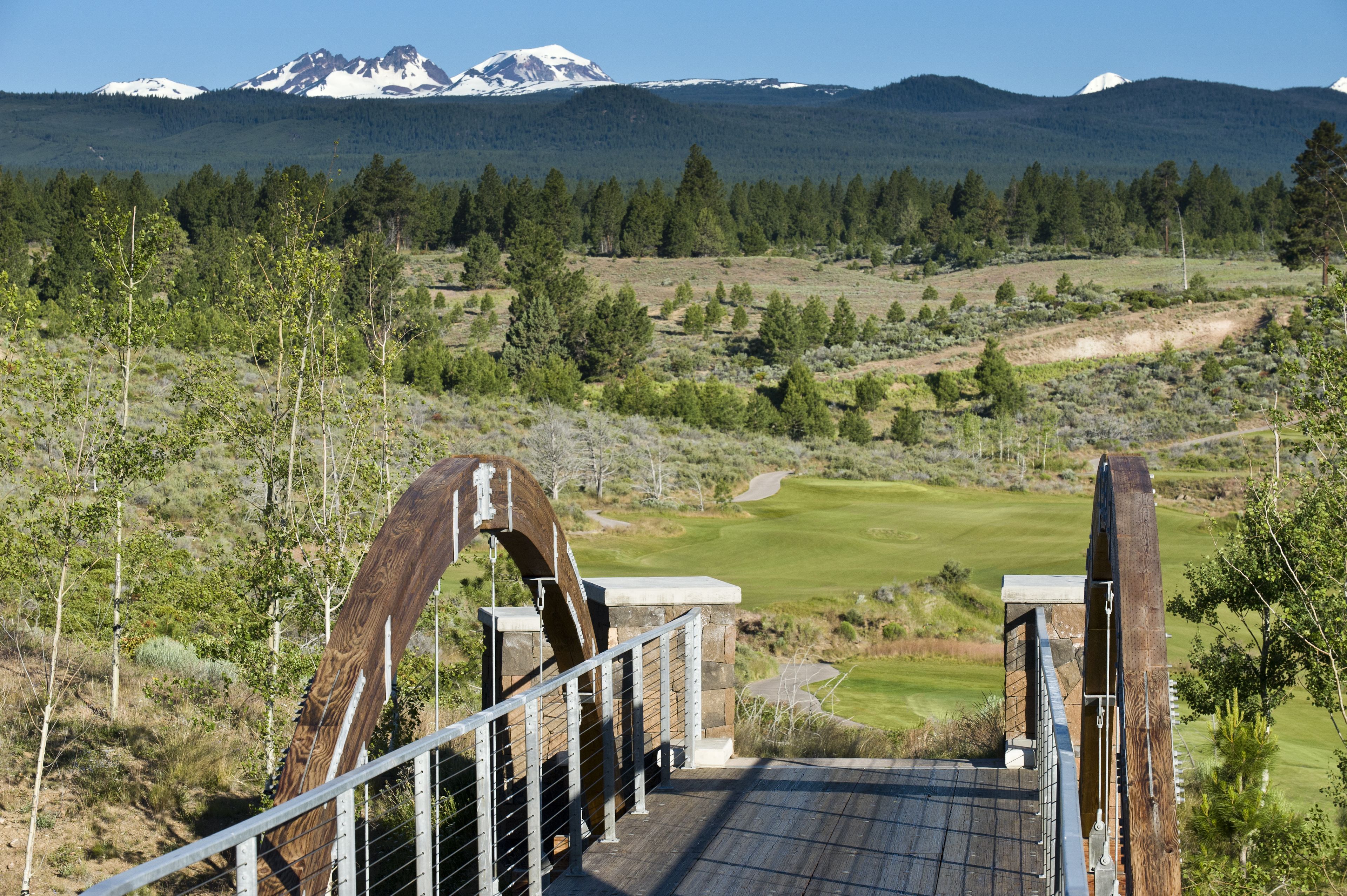 A wooden bridge leading to a golf course with a mountain backdrop.