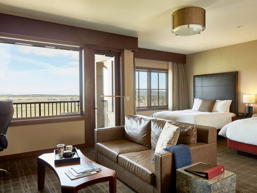A hotel room with a large window, a sofa, a desk, and two beds.
