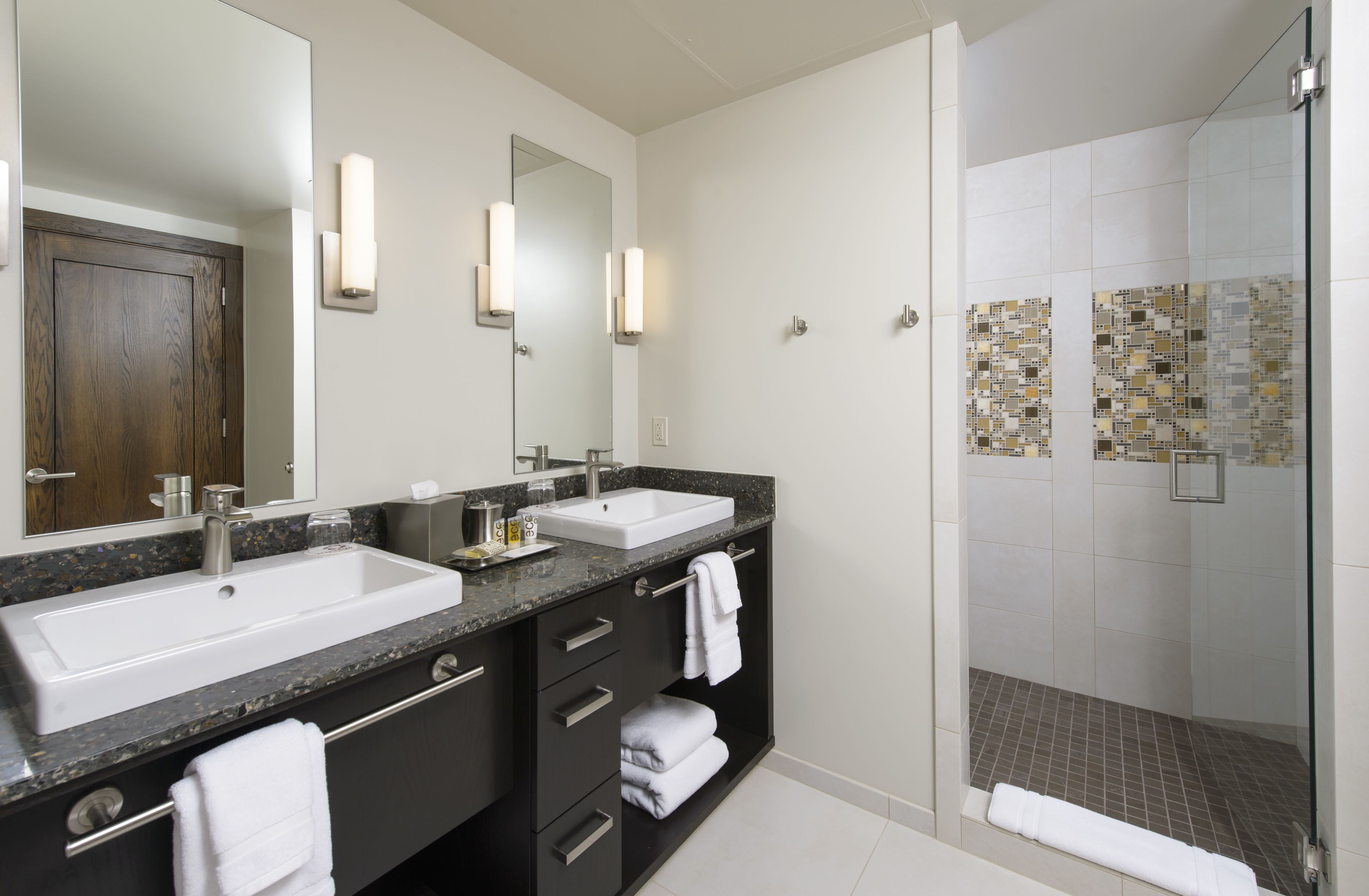 A modern bathroom with two sinks, dark cabinetry, and a glass shower enclosure.