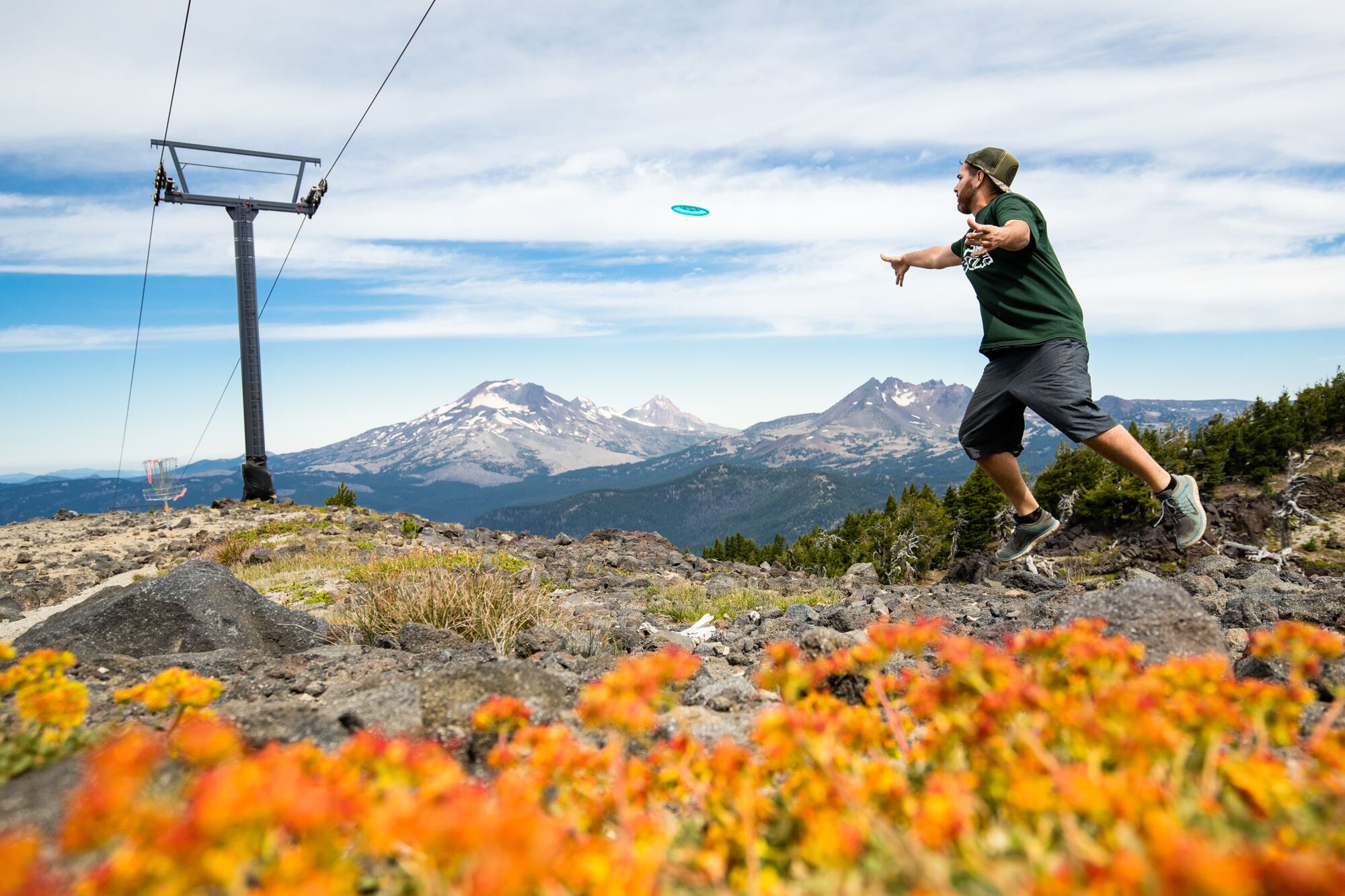 Uma pessoa jogando frisbee numa montanha, com vista desobstruída para montanhas cobertas de neve ao fundo.