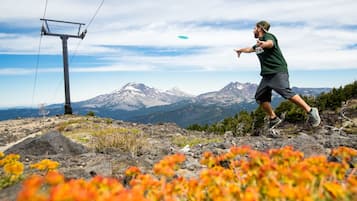 A person playing frisbee on a mountain with a clear view of snow-capped mountains in the background.