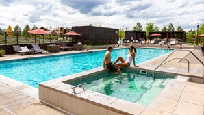 A swimming pool with lounge chairs and umbrellas, surrounded by a landscaped area with trees and a building in the background. - Tetherow Resort (Bend)