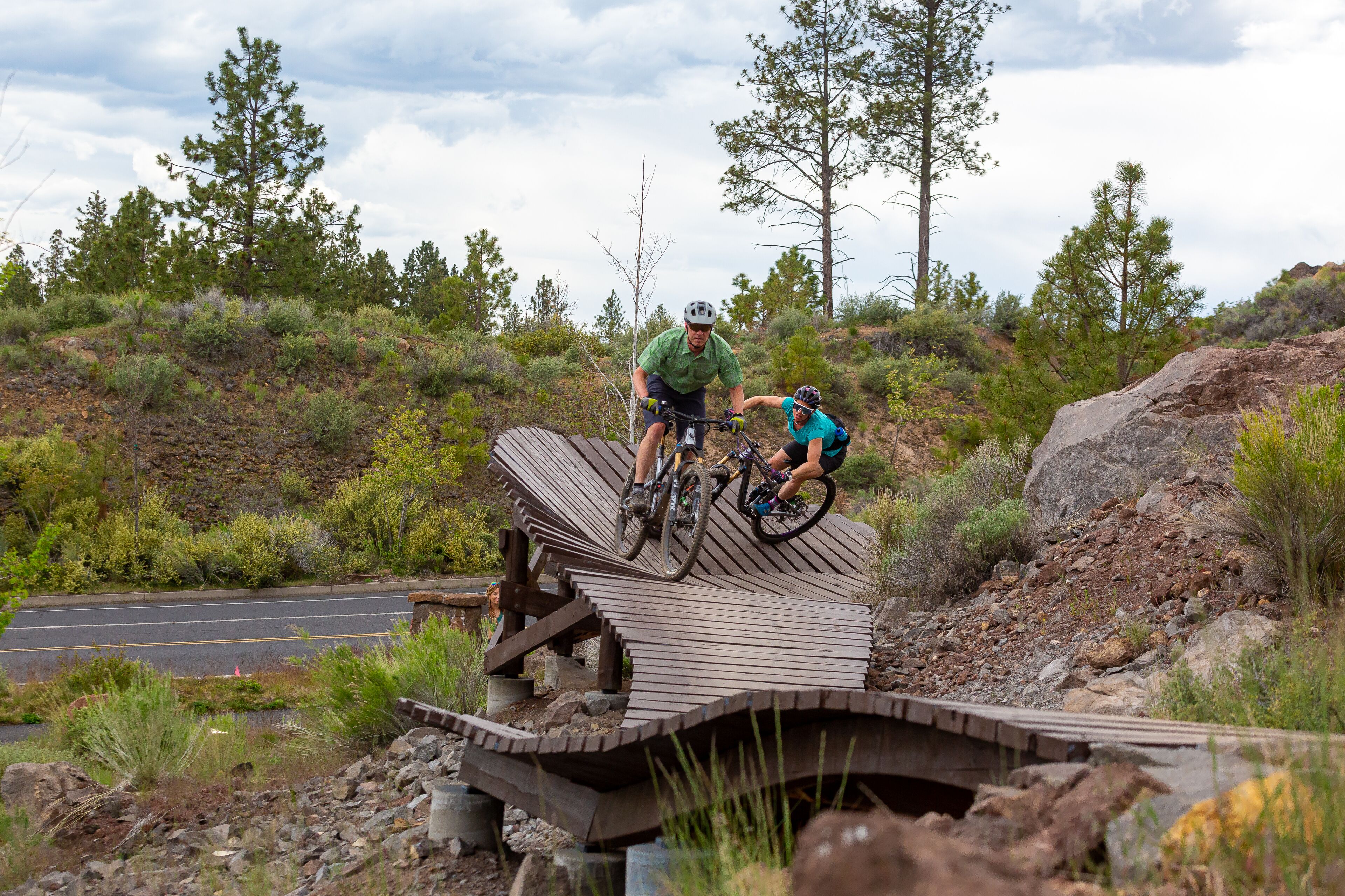 A wooden bridge with a metal railing, surrounded by rocky terrain and sparse vegetation.