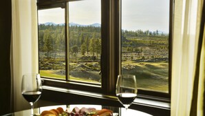 A table with a fruit platter and two wine glasses, a window with a view of a forest and mountains. - Tetherow Resort (Bend)