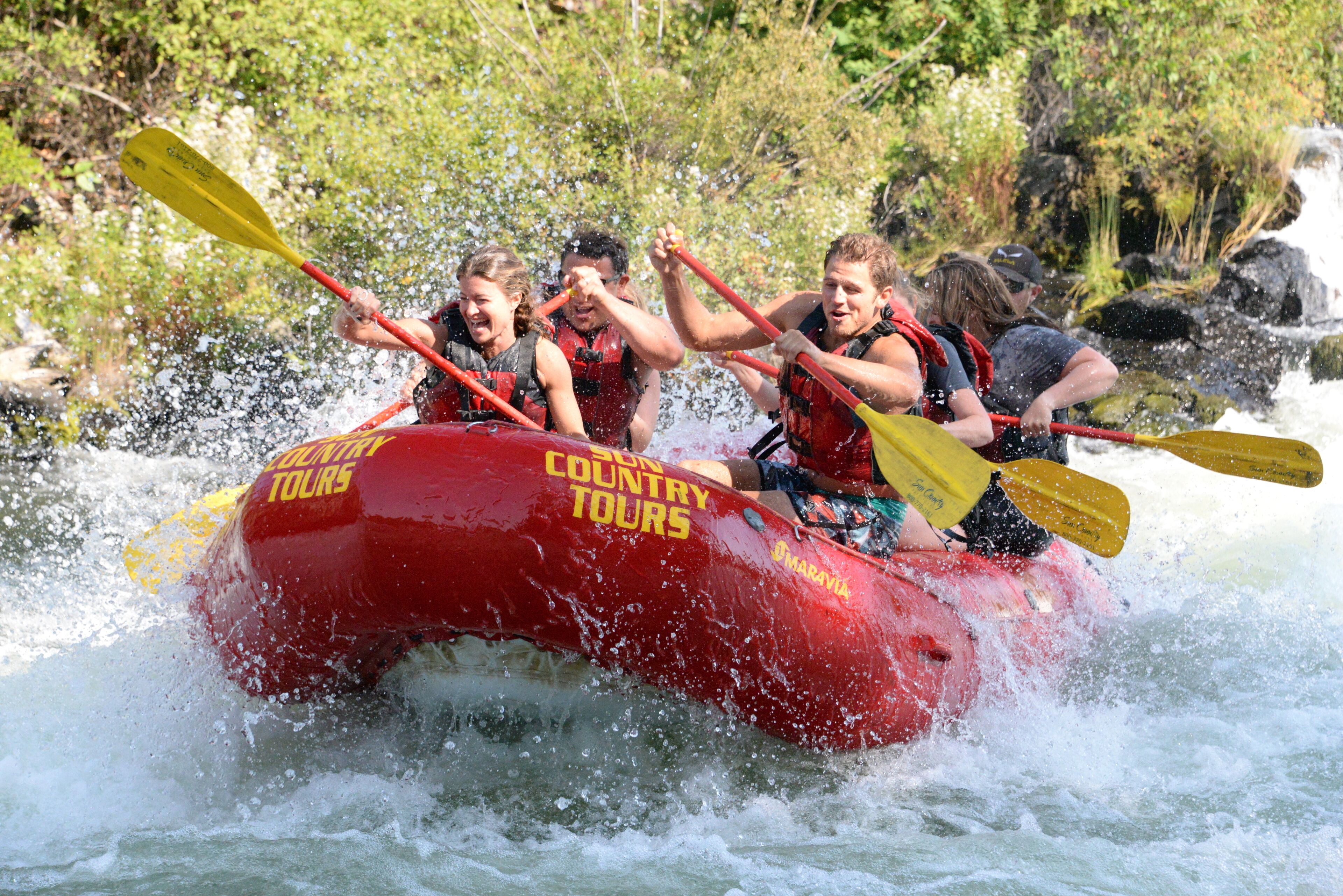 A group of people in a red raft with "COUNTRY TOURS" written on it, paddling through a river.