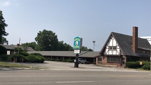 A building with a sign for Lincoln Lodge, featuring a large sign with a lion emblem, a parking lot, and a small parking garage. - Lincoln Lodge (Urbana)