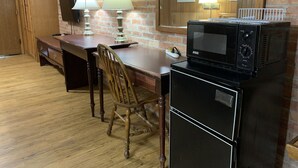 A compact kitchen with a microwave, a wooden desk, two lamps, and a chair. - Lincoln Lodge (Urbana)