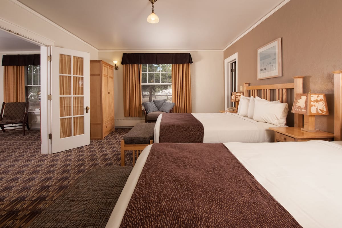 Une chambre d’hôtel avec deux lits, un bureau, une chaise, une armoire et une fenêtre avec des rideaux.