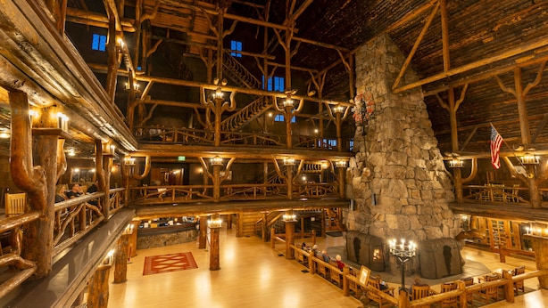 Un intérieur de chalet spacieux, doté d’une cheminée en pierre, de poutres en bois et de plusieurs coins salon.